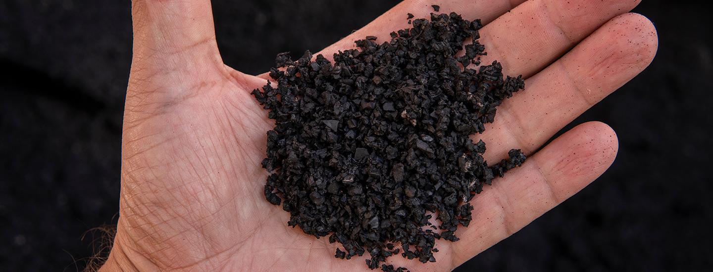Close-up of a hand holding recycled rubber granules used in Ecore flooring, showing texture and details.